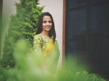 Portrait of smiling young woman standing against plants