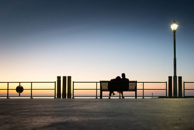 Silhouette people on street light against clear sky during sunset