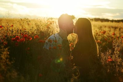 Young couple on poppy field against sky during sunset