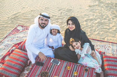 Portrait of happy family sitting on carpet at desert 