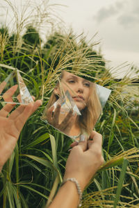 Reflection of woman looking away and holding prism in mirror against plants