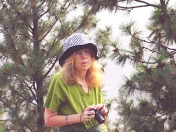 Portrait of woman with camera wearing hat against trees
