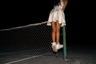 Low section of woman standing on fence at night