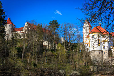 Low angle view of trees and buildings against blue sky