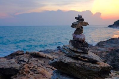 Stack of rocks on shore against sea during sunset