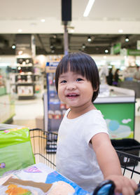 Portrait of girl smiling while sitting in shopping cart at supermarket