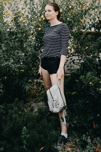 Full length of smiling young woman standing with bag
