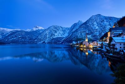 Buildings by lake in town at dusk during winter