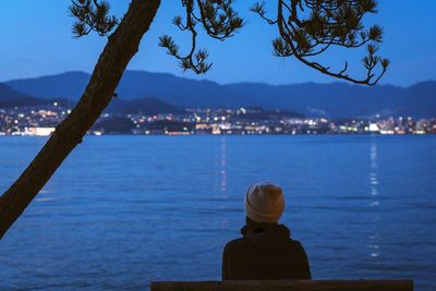 Rear view of woman looking at sea while sitting on bench against sky