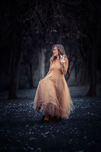 Full length of woman wearing beige dress while walking in forest