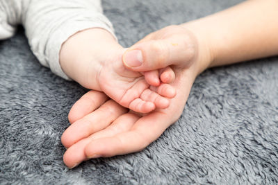 Cropped image of mother and baby holding hands on rug