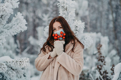 Portrait of woman wearing mask with ornaments standing against trees during winter