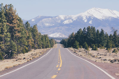 Empty road amidst trees leading towards mountains on sunny day