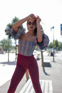 Portrait of fashionable young woman standing on road in city during sunny day