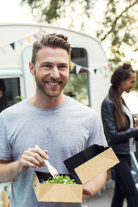 Happy male customer holding disposable salad box against food truck