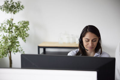 Smiling mid adult businesswoman using headset in office in front of computer screen