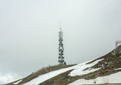 Low angle view of communications tower on hill against sky