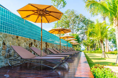 Empty chairs by swimming pool against sky