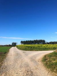 Dirt road along landscape and against clear blue sky