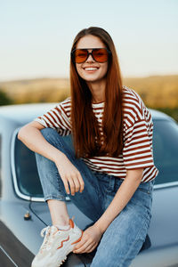 Portrait of young woman sitting on car