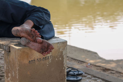 Low section of man with dirty feet relaxing on bench by pond