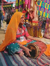 Full length of senior woman playing drum sitting at market