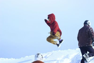 Low angle view of people jumping on snow against clear sky