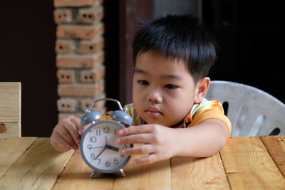 Cute boy playing with alarm clock at table