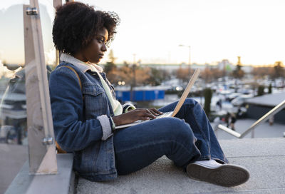 Young woman using laptop sitting on staircase at sunset