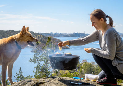 Side view of woman preparing food by dog on cliff