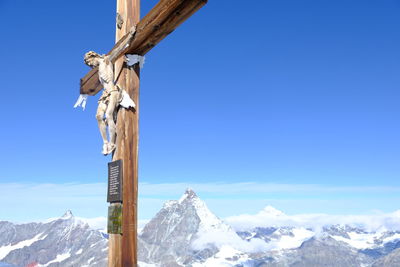 Cross on snow covered mountain against blue sky