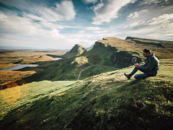 Panoramic view of man sitting on mountain against sky