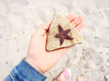 Close-up of hand holding rock on sand at beach