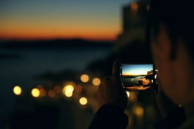 Close-up of hand holding camera at beach against sky at night