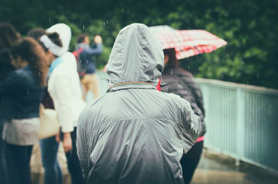 Rear view of person wearing raincoat while standing outdoors during rainfall