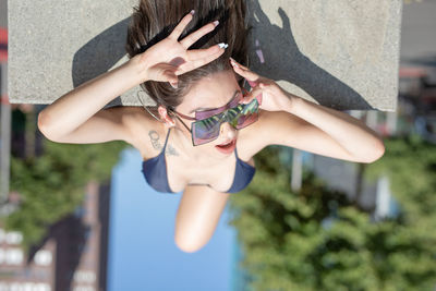 Fashionable young woman wearing sunglasses and bikini while lying on road in city during sunny day