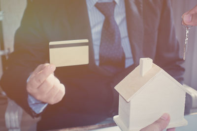 Midsection of businessman with credit card by colleague holding model home and keys