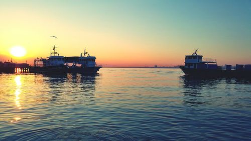 Boats sailing in sea against clear sky during sunset