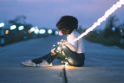 Woman with illuminated string light on road at night