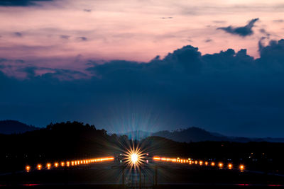 Illuminated airplane at airport runway against cloudy sky at dusk
