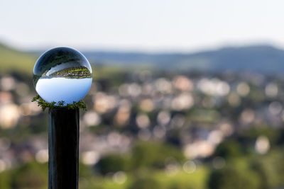 Close-up of crystal ball on wooden post against sky