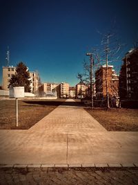 Empty footpath by buildings against blue sky