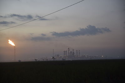 Fire emitting from smoke stack at industrial site against sky