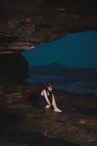 Woman sitting on rock by sea