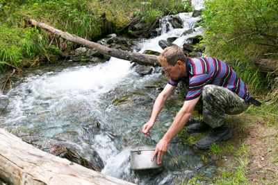 Man filing water in utensil from river