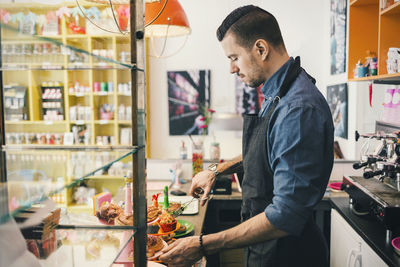 Side view of male barista using tongs to remove cupcake at cafe counter