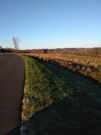 Road amidst field against clear sky