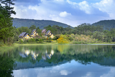 Scenic view of lake by trees and houses against sky