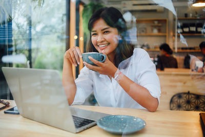 Portrait of smiling businesswoman drinking coffee while using technology in cafe