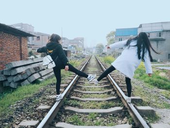 Full length rear view of friends balancing on railroad track against sky